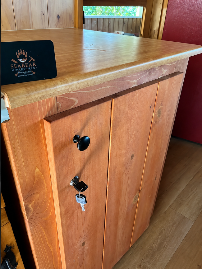 Wooden cabinet with black knobs and a key lock in a cabin-style room.