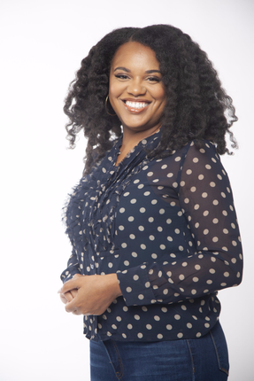 A woman with curly hair is wearing a blue polka dot shirt and jeans.