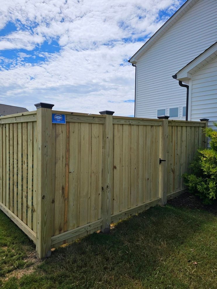 Wooden fence enclosure beside a white house under a partly cloudy sky