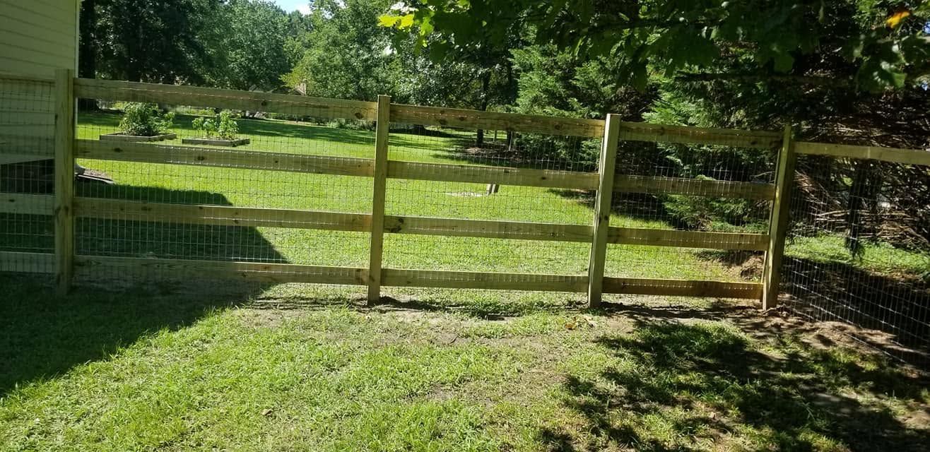 Wooden fence beside a grassy yard with trees and sunlight in the background