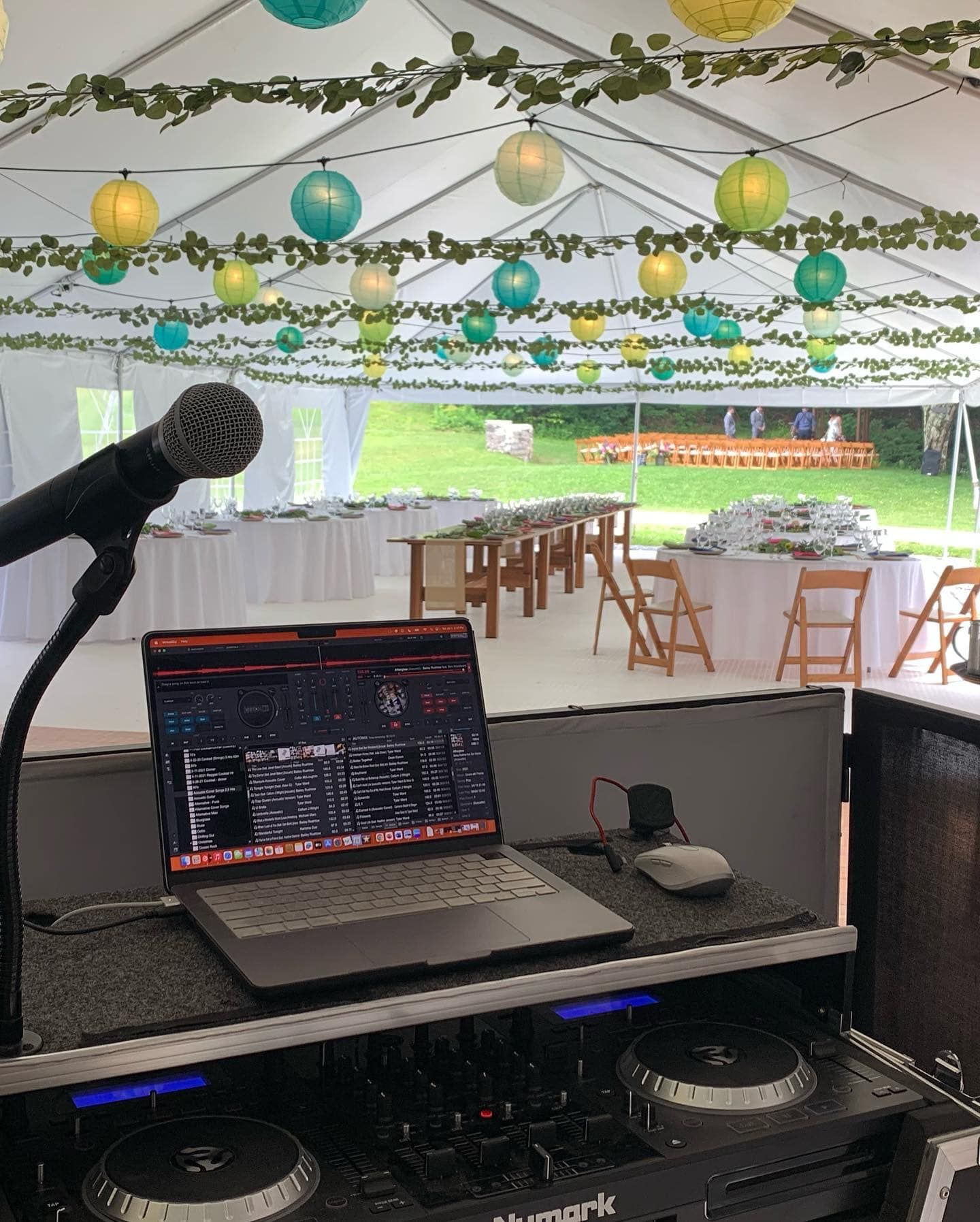 DJ setup with laptop and microphone inside a decorated tent, tables and chairs visible.