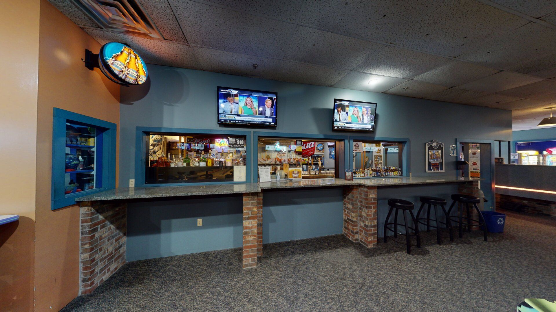 Bar area with counter, stools, TVs, and popcorn sign, in a bowling alley setting.