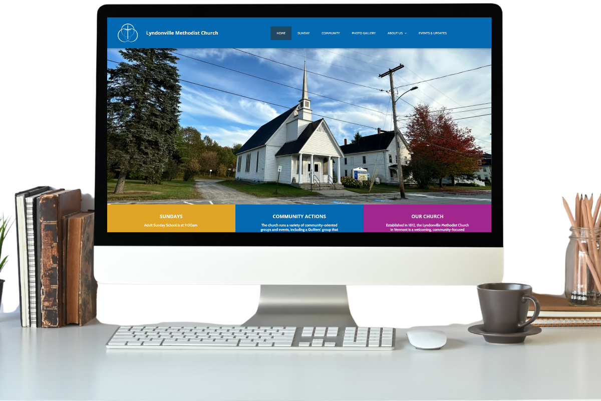 Desktop computer displaying a church website on a desk with books, a coffee cup, and pencils