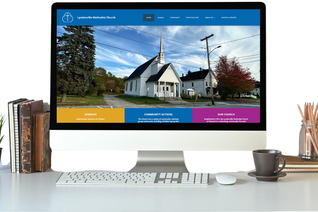 Desktop computer displaying a church website on a desk with books, a coffee cup, and pencils