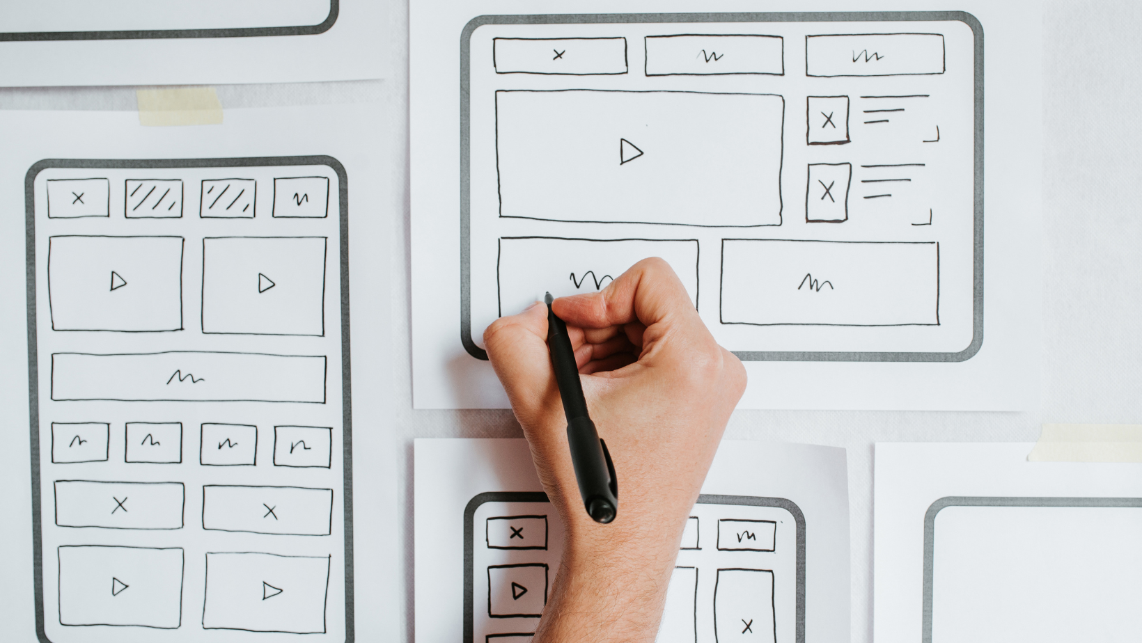 A person is drawing website layouts on a piece of paper with a pen.
