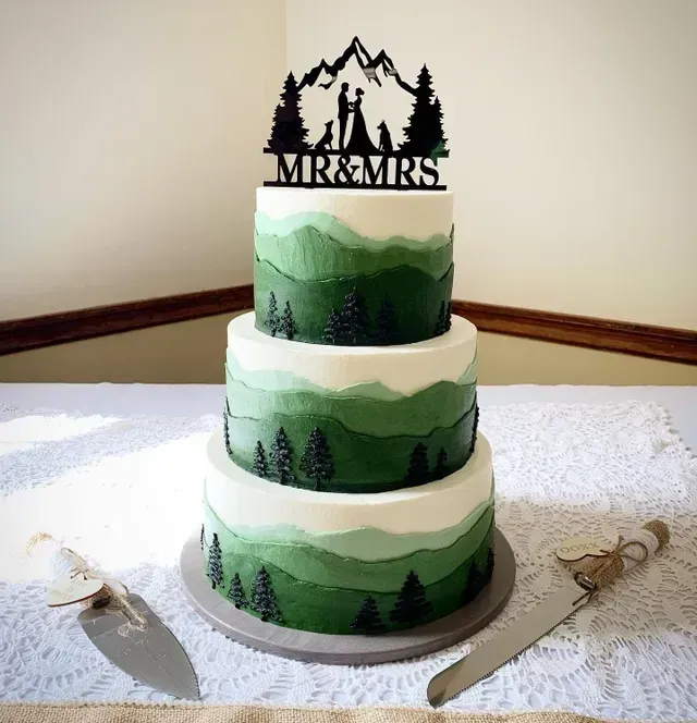 Three-tiered wedding cake with green mountain scene and