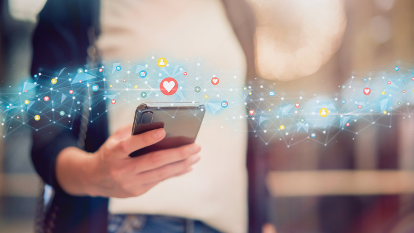 A person is holding a cell phone in their hand with emojis coming out of it.