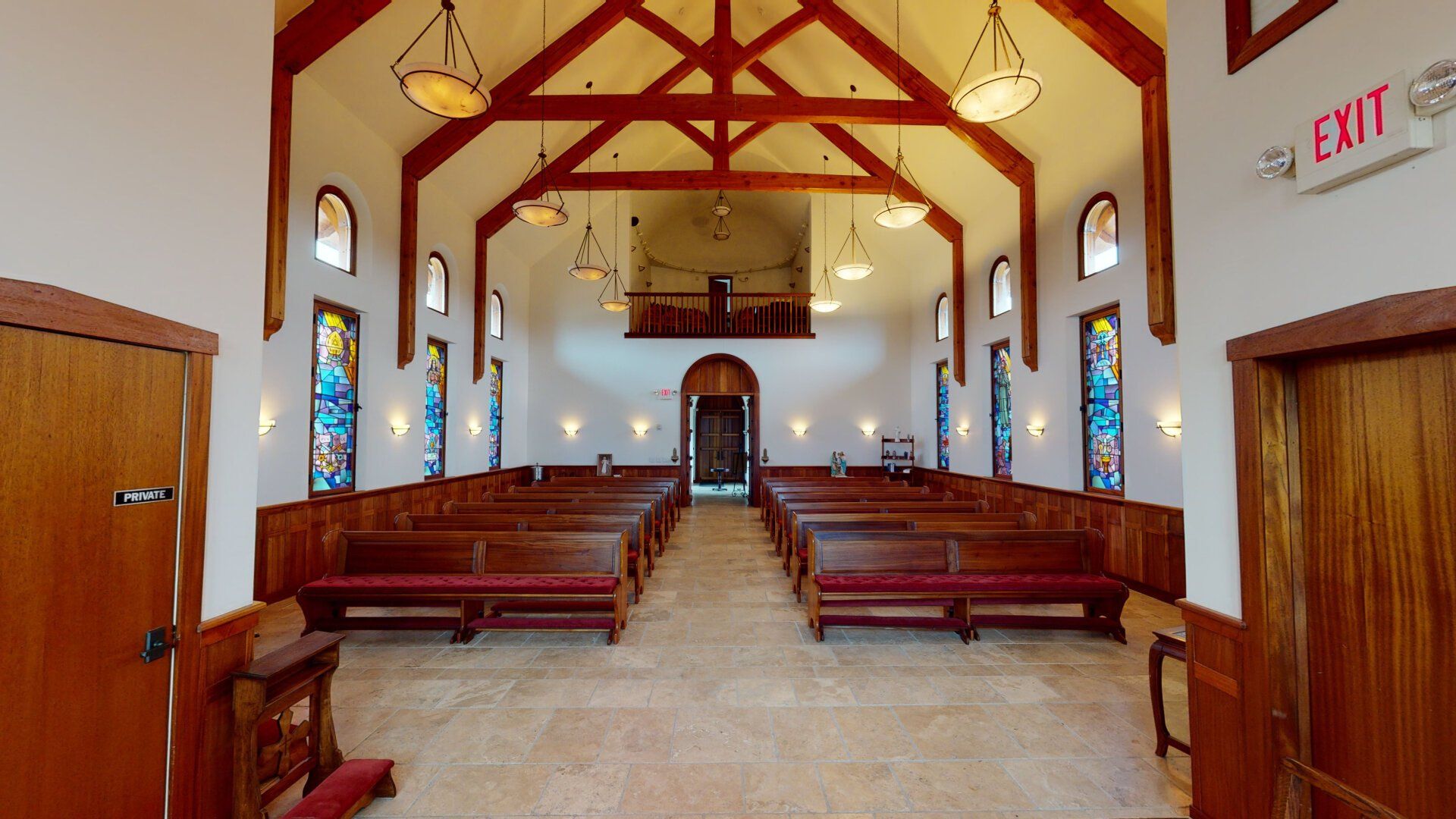Interior of a chapel with wooden pews, stained glass windows, and a vaulted ceiling.
