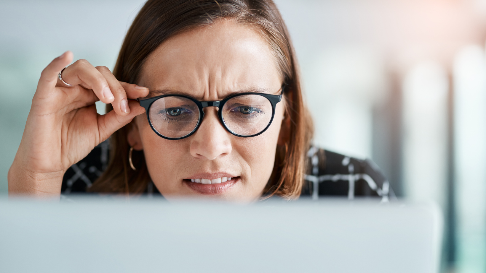 A woman wearing glasses is looking at a computer screen confused.