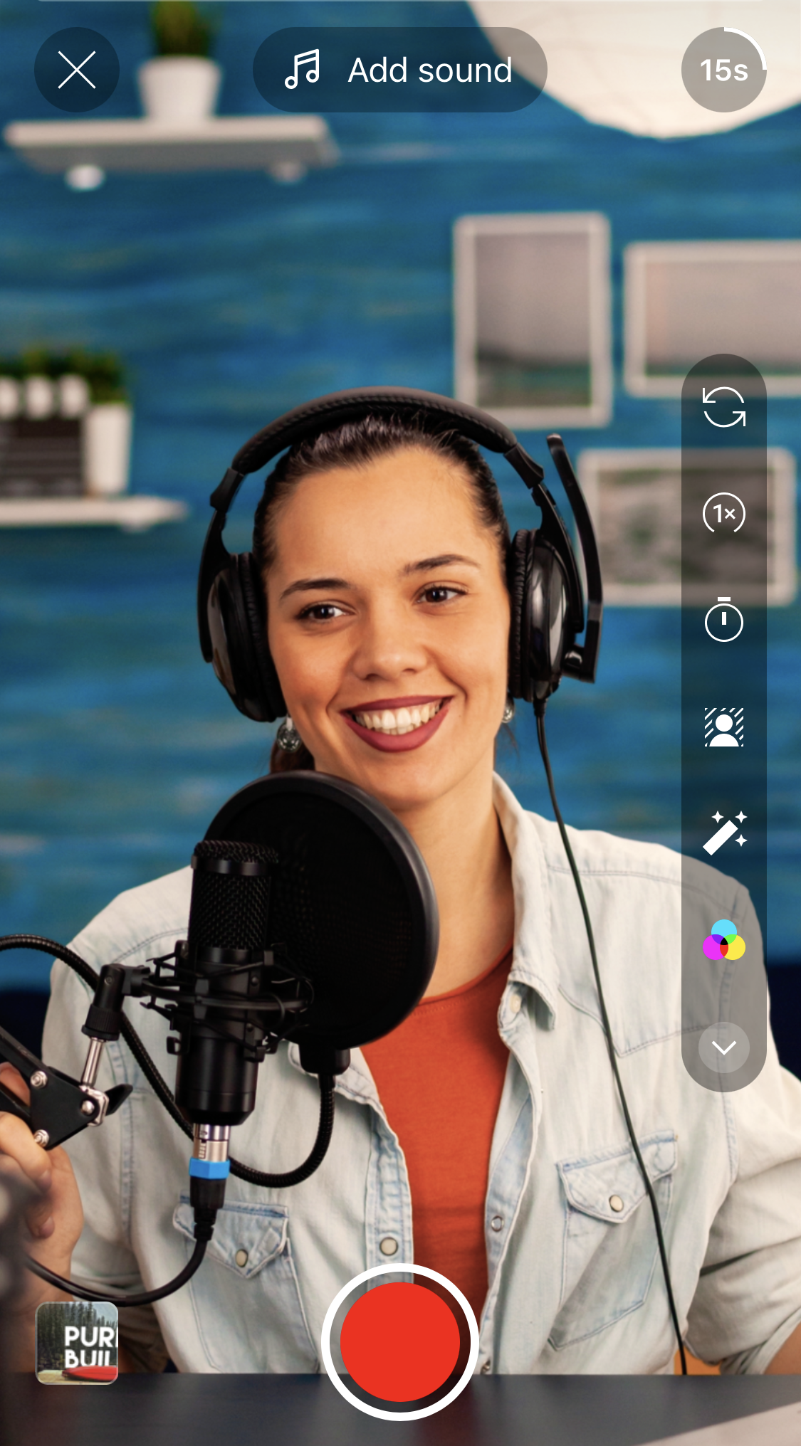 Woman wearing headphones, recording into a microphone, smiling, inside a studio. The camera interface is visible.