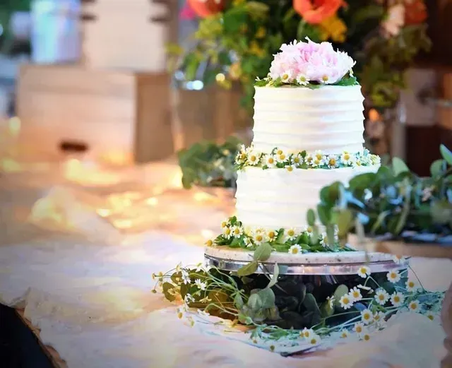 Three-tiered white cake with floral decorations on a table, with greenery.