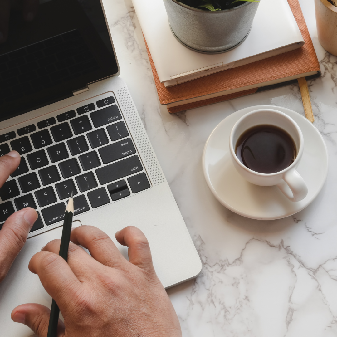A persons hands working on a laptop with a cup of coffee next to it