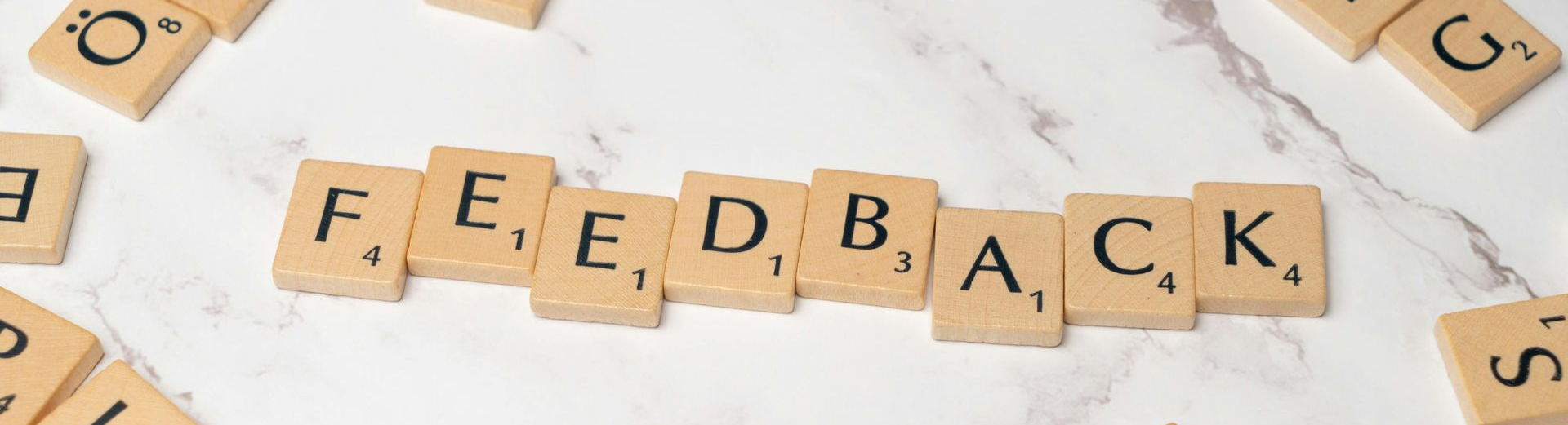 Wooden letter tiles spelling ‘FEEDBACK’ on a marble surface, representing communication and collaboration.