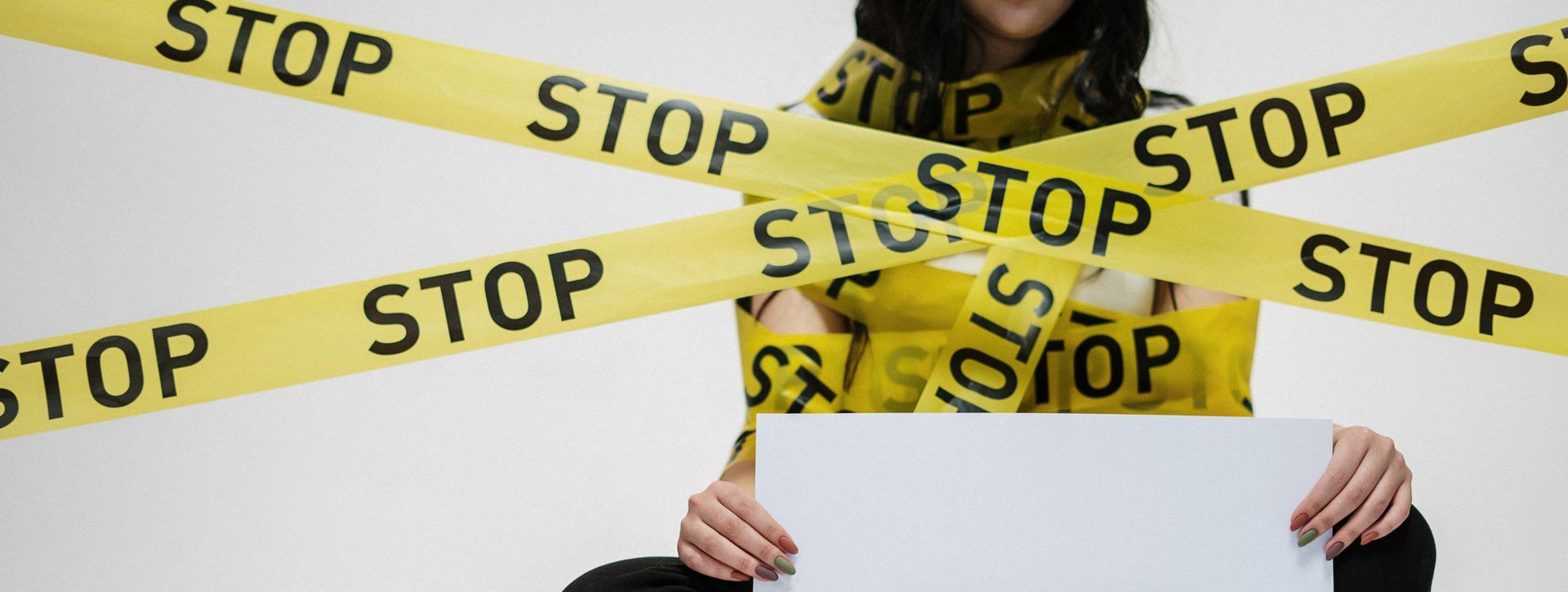 Woman looking at laptop, with a stop tape wrapped around her—signifying staying safe