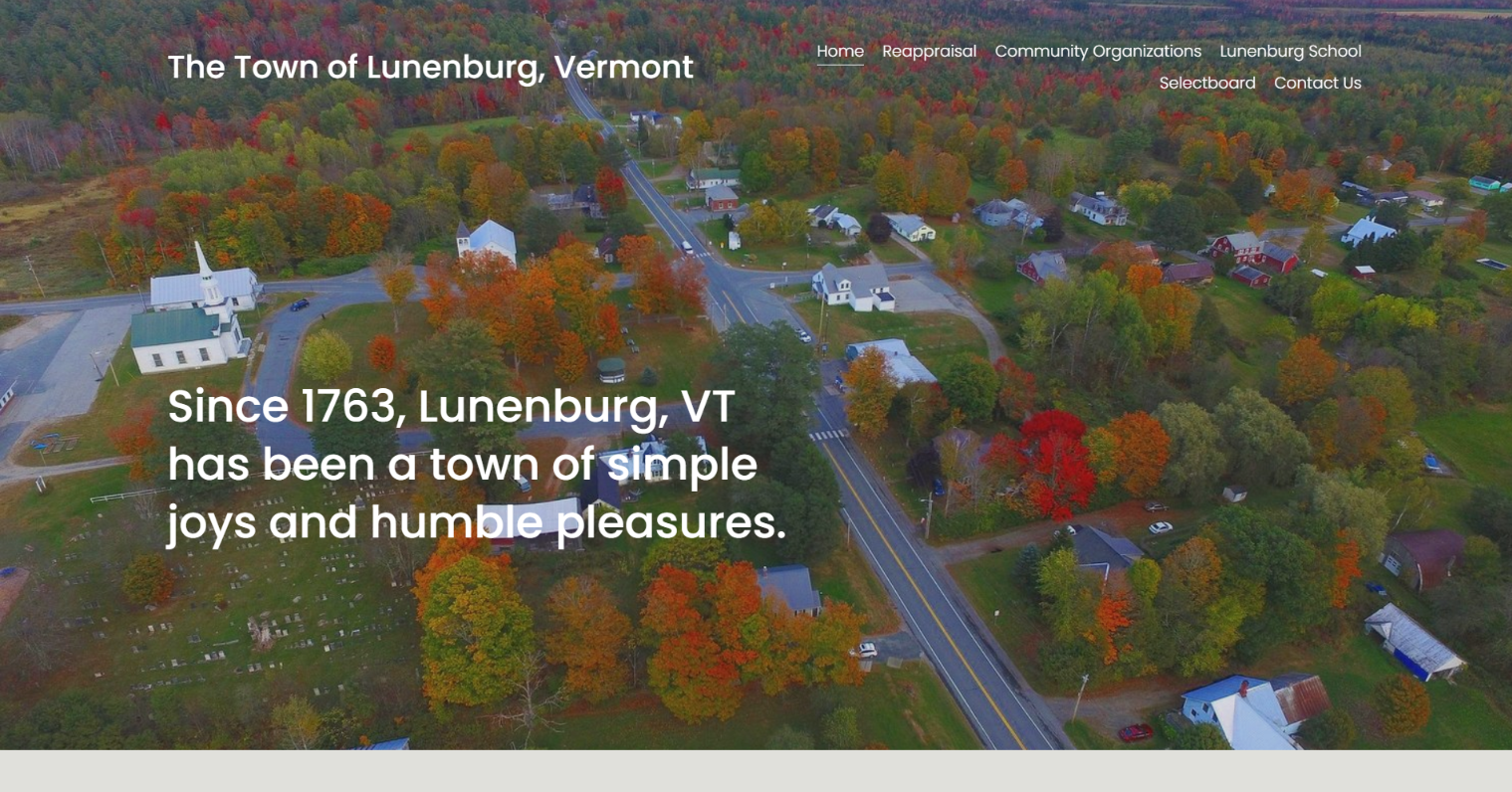 Aerial view of Lunenburg, Vermont, with fall foliage, buildings, and a road. Text reads: 