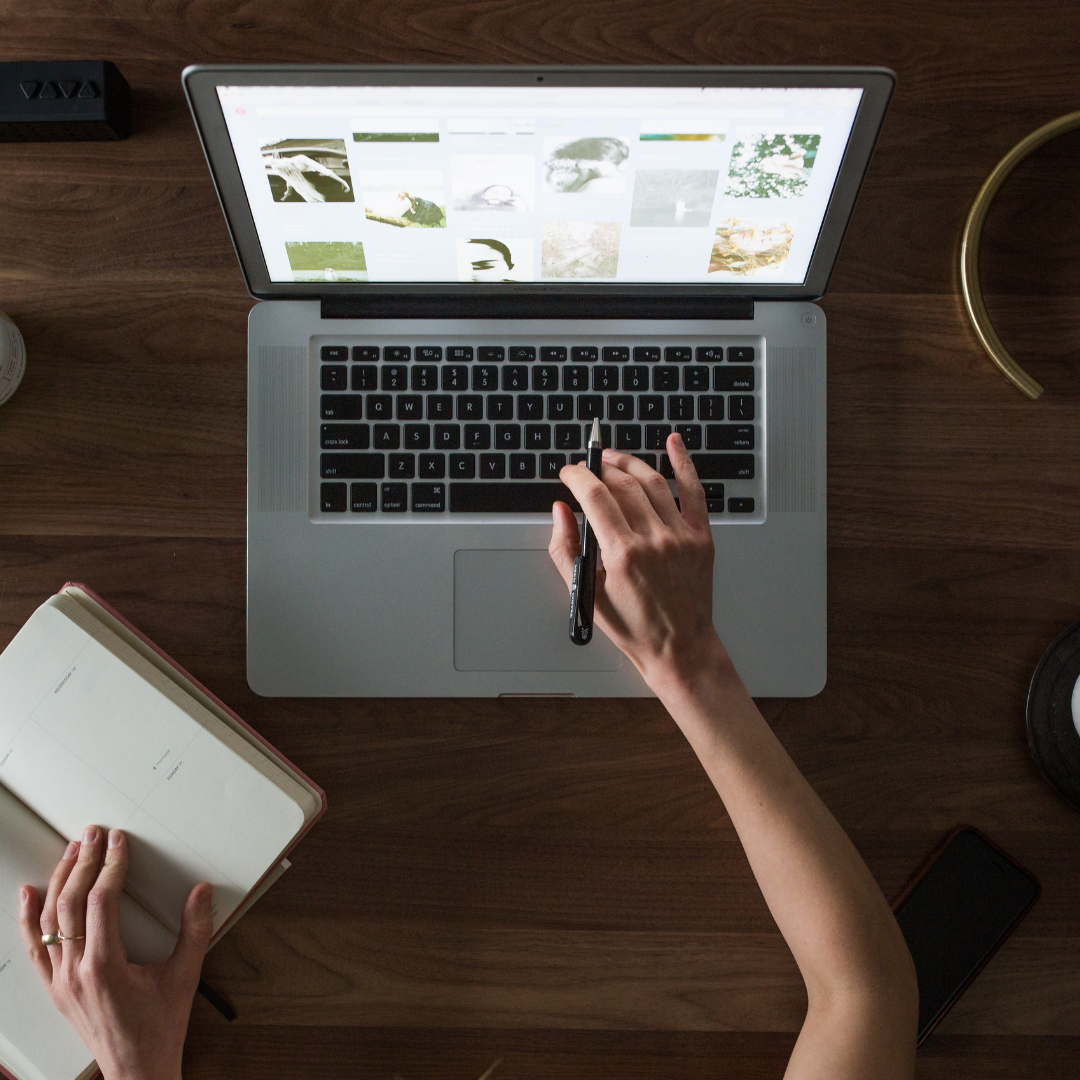 A persons hands designing a website on their laptop, while looking at notes taken
