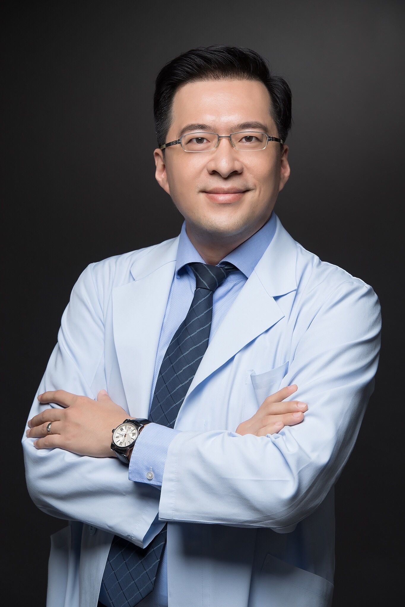 A man in a white coat and tie is standing with his arms crossed.