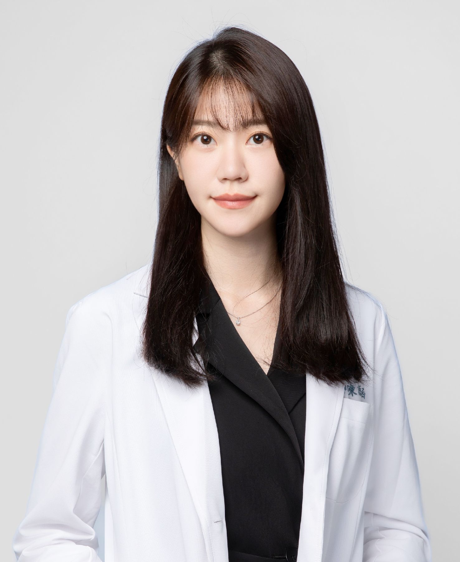 A woman in a white lab coat is sitting down with her hand on her chin.