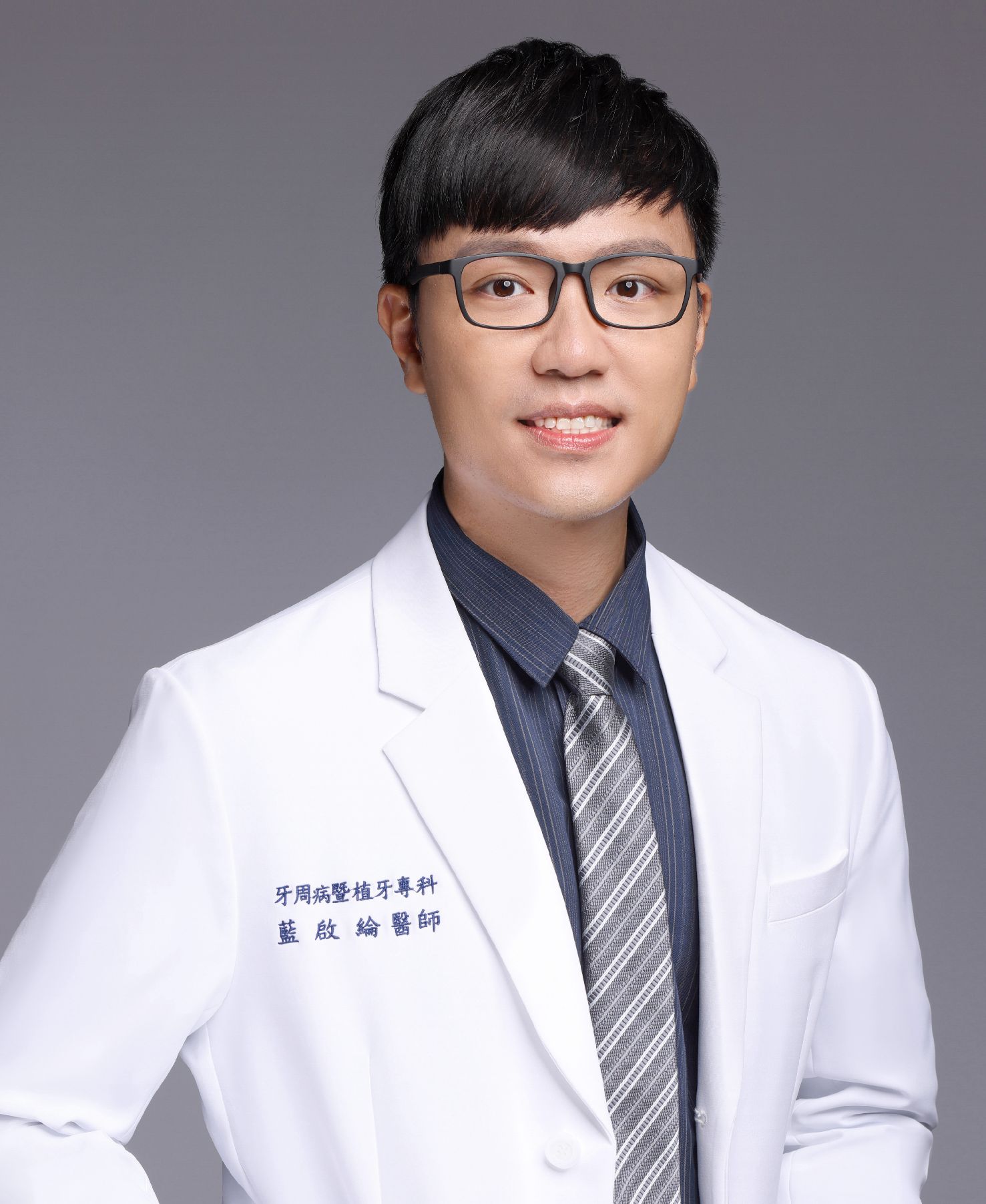 A young man in a lab coat and tie is smiling for the camera.