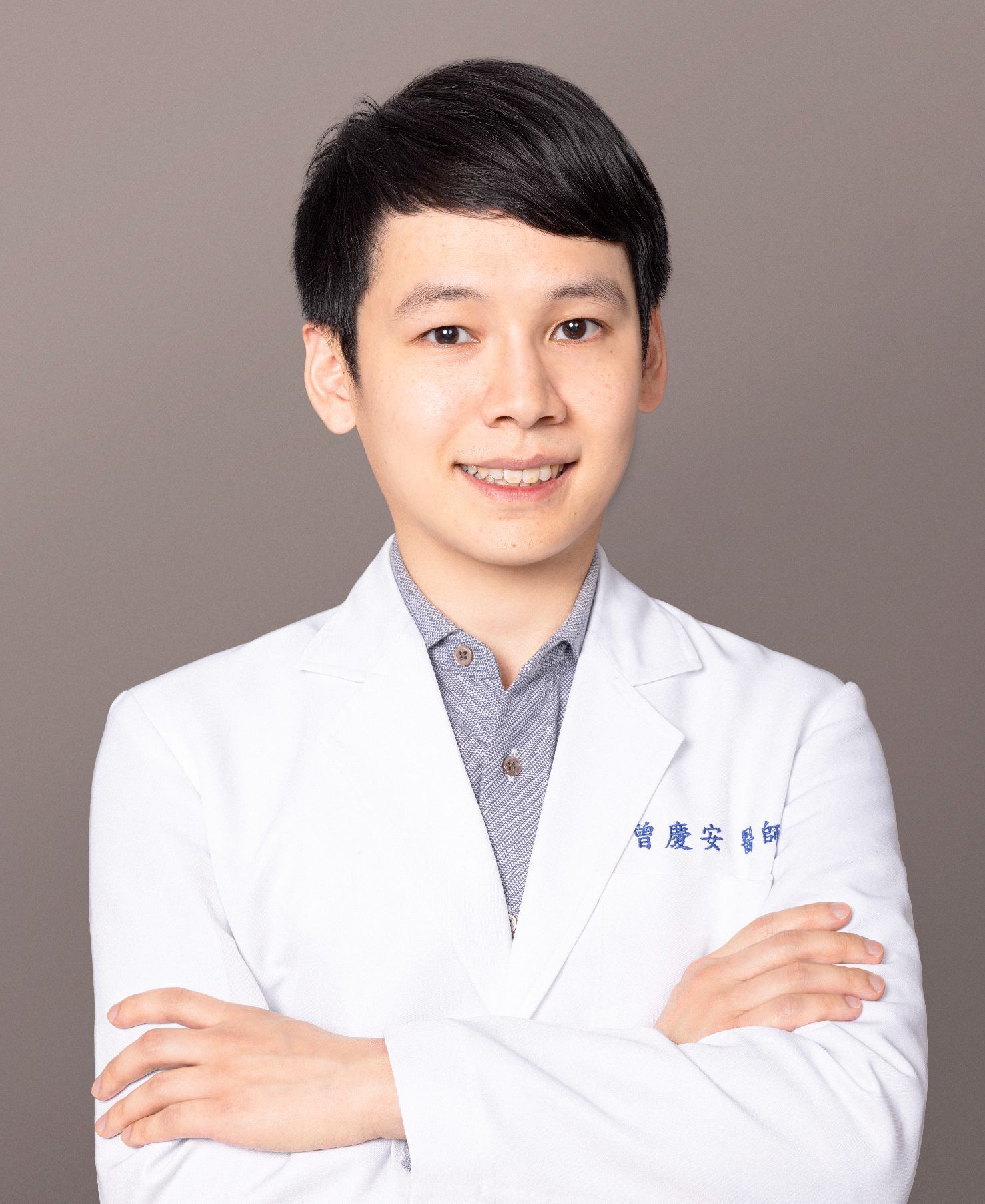 A young man in a white lab coat is standing with his arms crossed.