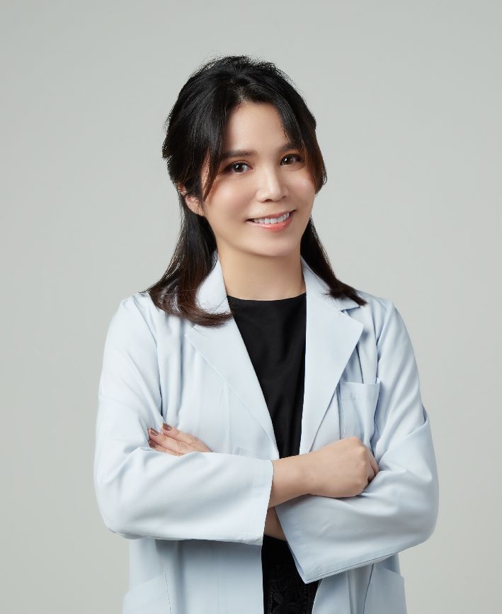 A woman in a white coat is standing with her arms crossed and smiling.