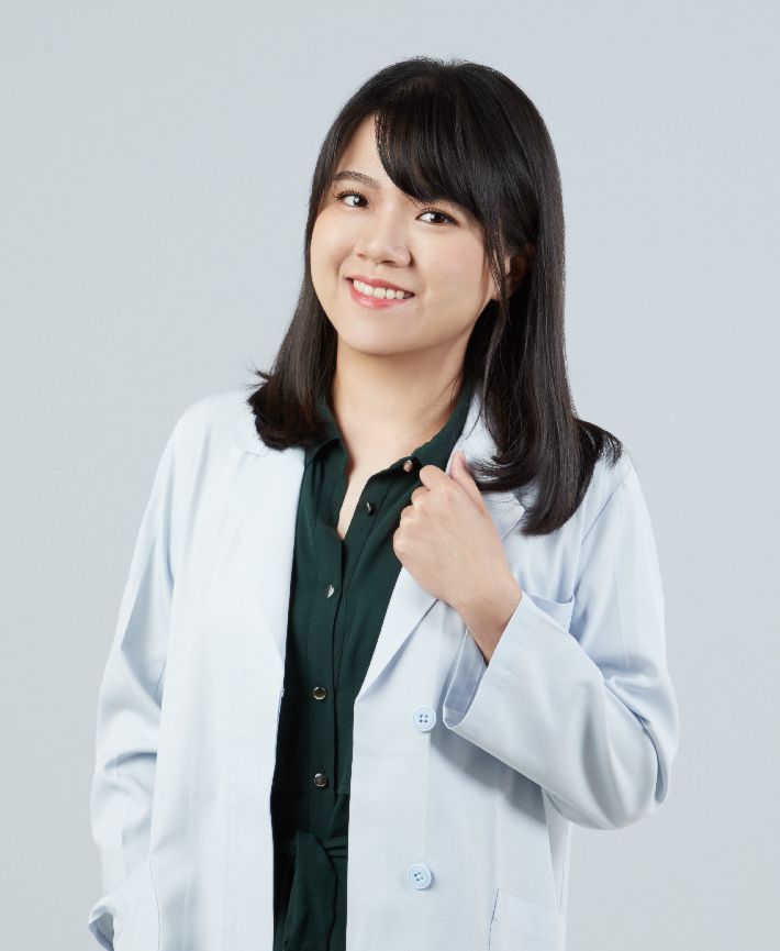 A woman in a white coat and green shirt is smiling.