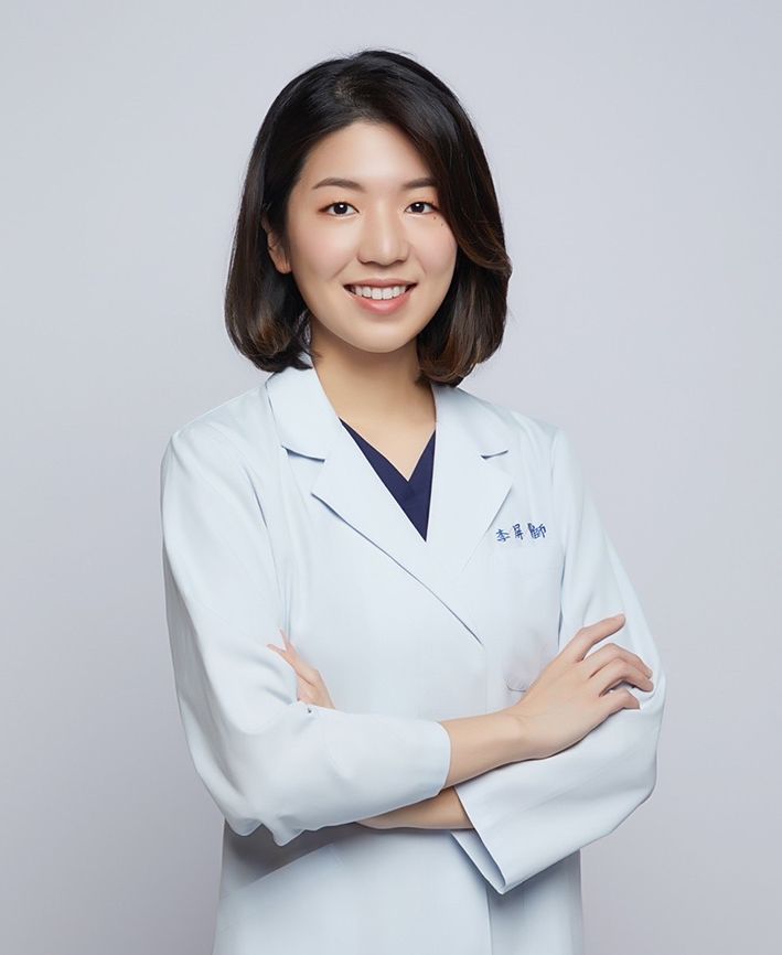 A woman in a white lab coat is smiling with her arms crossed.