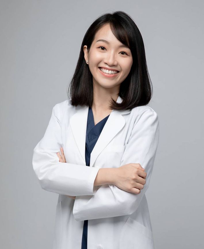 A woman in a lab coat is smiling with her arms crossed.