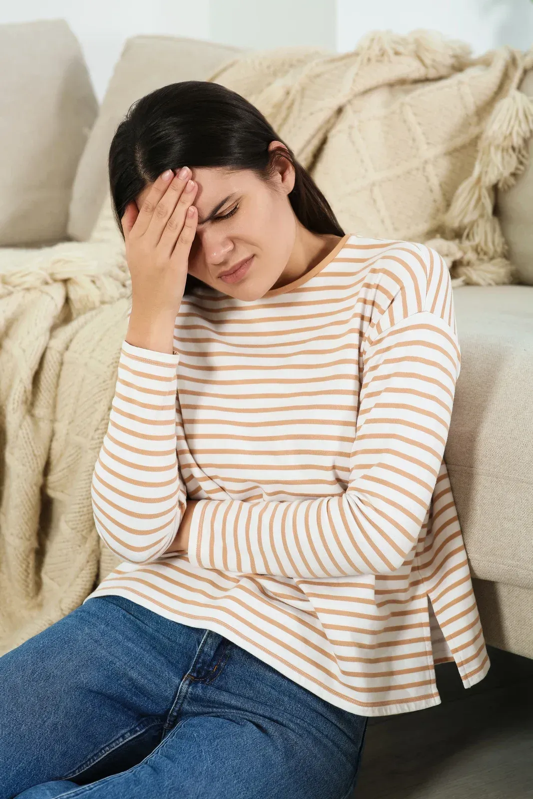 Woman with hand on forehead, sitting on floor, appears to be in pain.