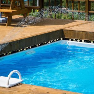 A swimming pool with a wooden deck and a picnic table in the background.