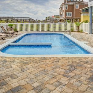 A large swimming pool is surrounded by a brick patio and chairs.