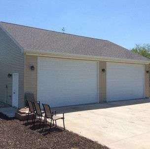 A garage with three white garage doors and chairs in front of it.