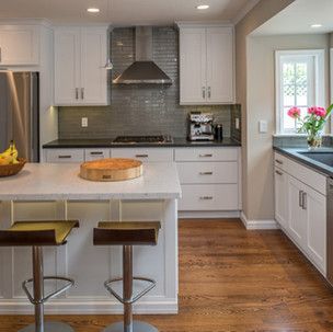 A kitchen with white cabinets , stainless steel appliances , hardwood floors and a large island.