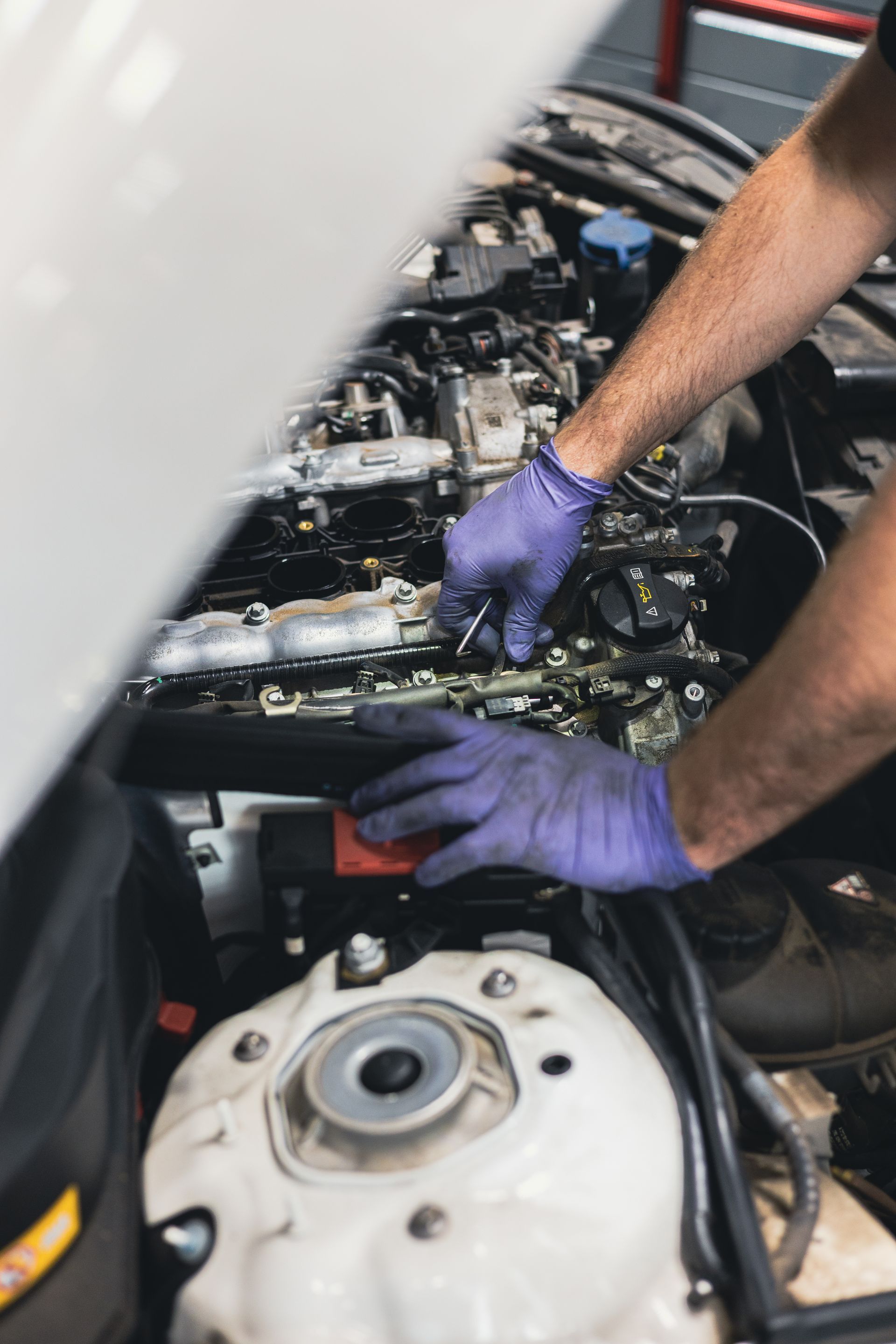 Mechanic wearing purple gloves working on an engine in a car bay