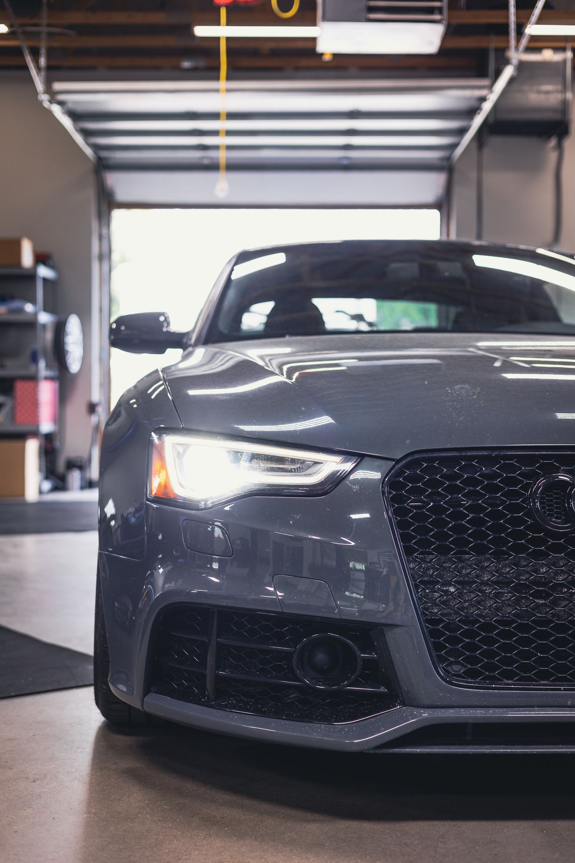 Gray sports car parked in a garage, front view with headlights on