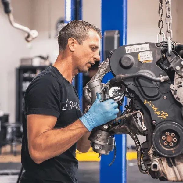 Mechanic in blue gloves inspecting a car engine in an auto repair shop