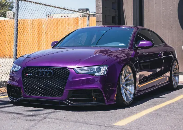 Purple Audi sedan parked outdoors in sunlight beside a chain-link fence
