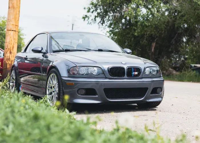 Gray BMW sedan parked on a driveway beside greenery and a wooden post