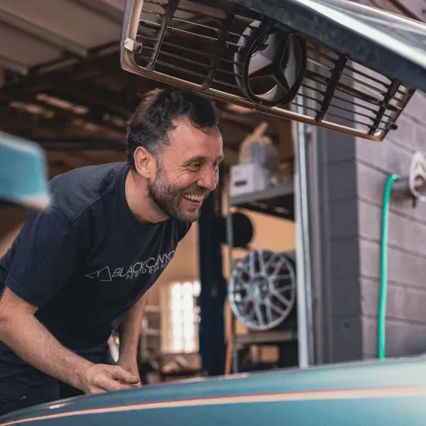 Smiling man leaning over a car hood in a garage, inspecting the engine.