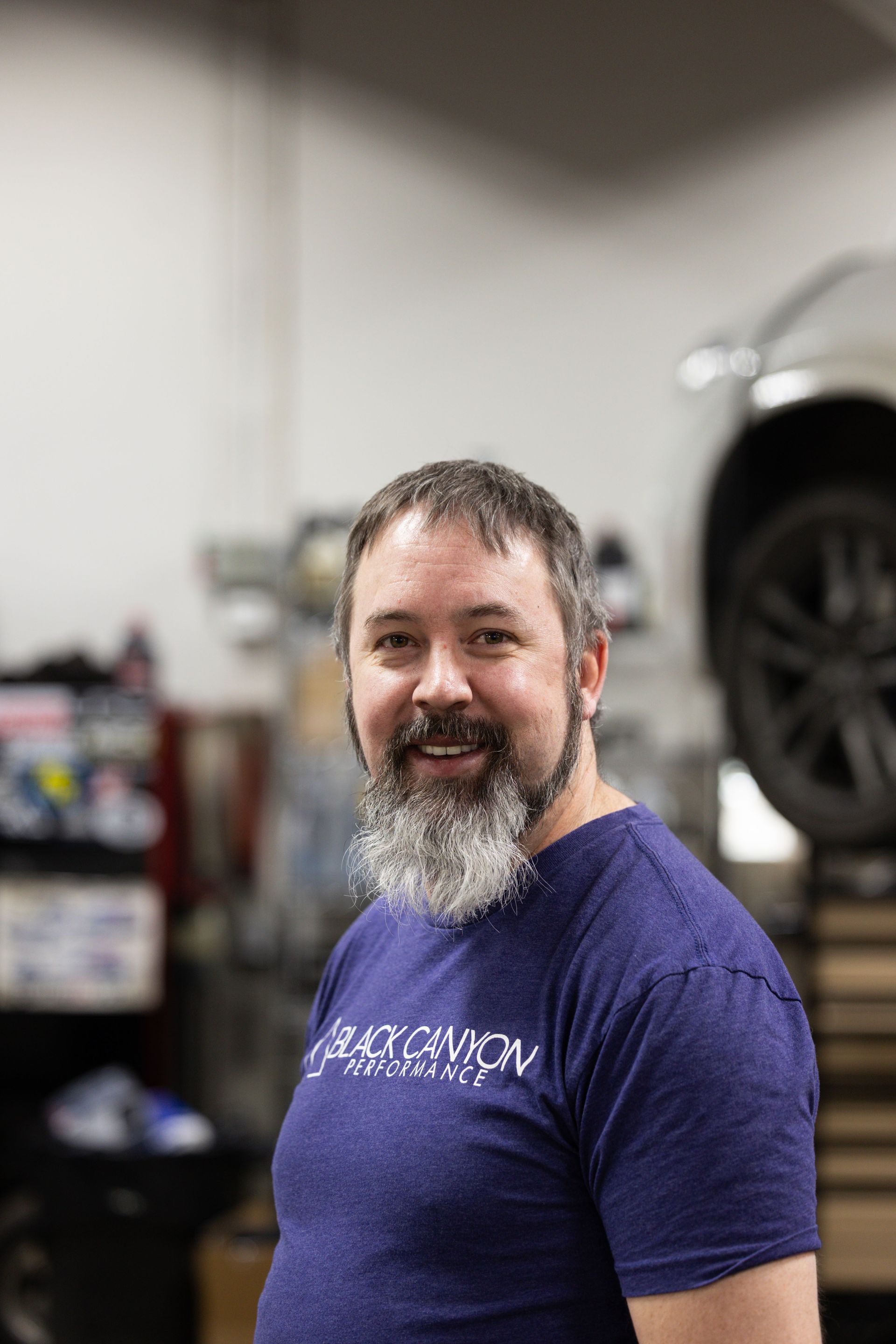 Smiling person in a purple T-shirt standing in a garage with a car in the background