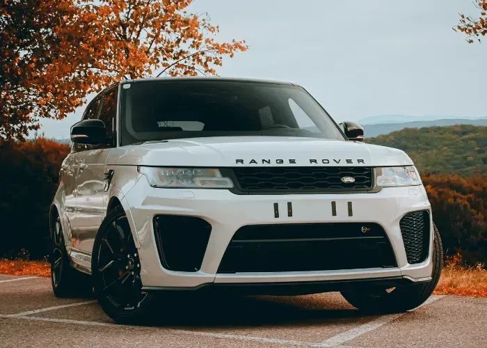 White Range Rover parked on a road beside autumn trees and hills