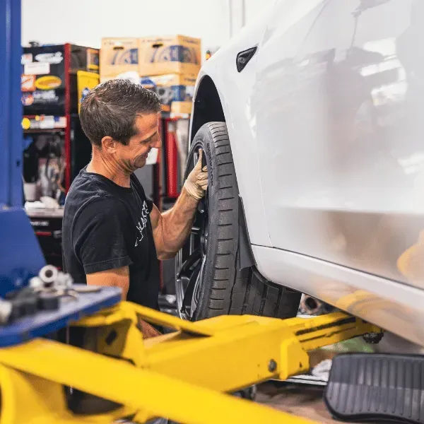 Mechanic inspecting a white car’s wheel in an auto repair shop