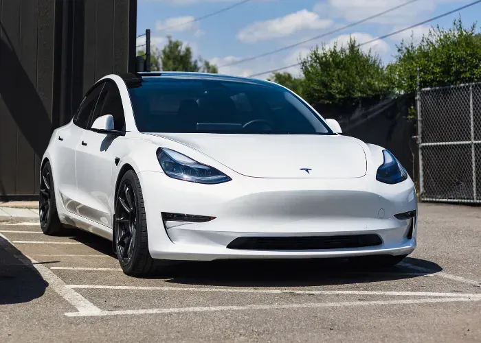 White Tesla Model 3 parked outdoors beside a building on a sunny day