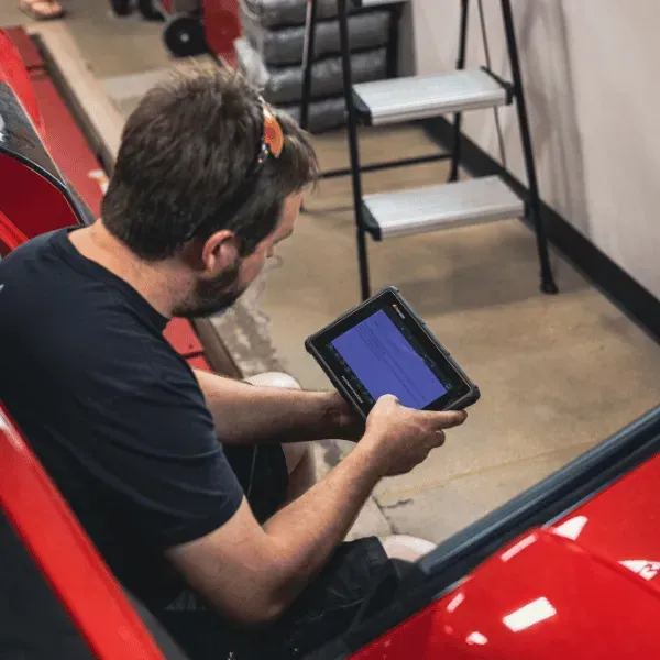 Man sitting beside a red car, using a tablet in a workshop area