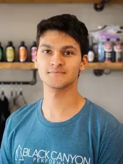 Portrait of a person in a blue Black Canyon T-shirt standing indoors with shelves of bottles behind them