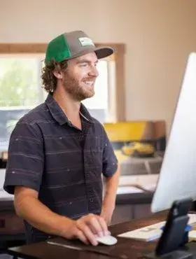 Smiling man in a green cap using a desktop computer at a desk in an office