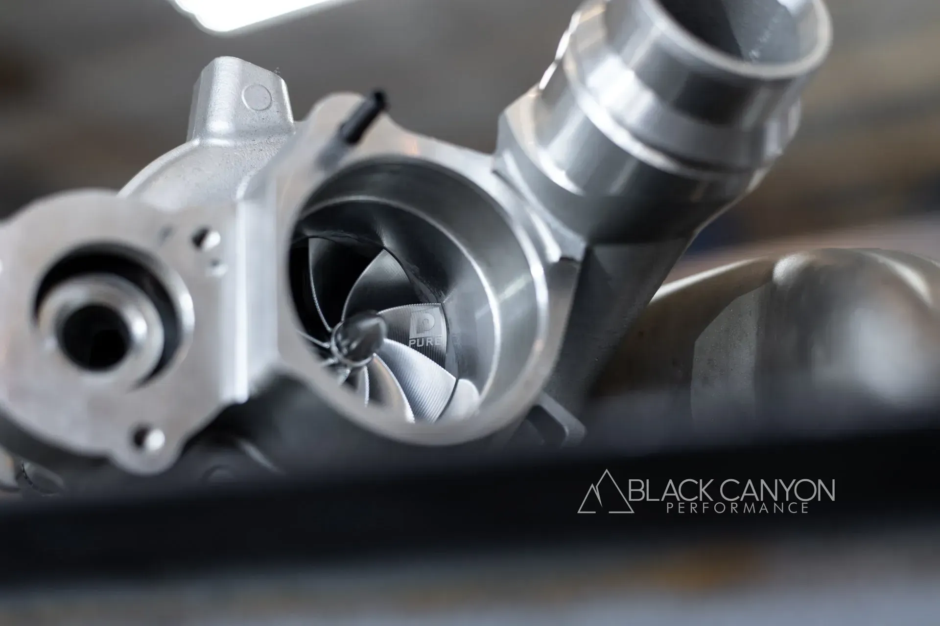 Close-up of a metallic engine turbocharger with polished turbine blades and black canyon watermark