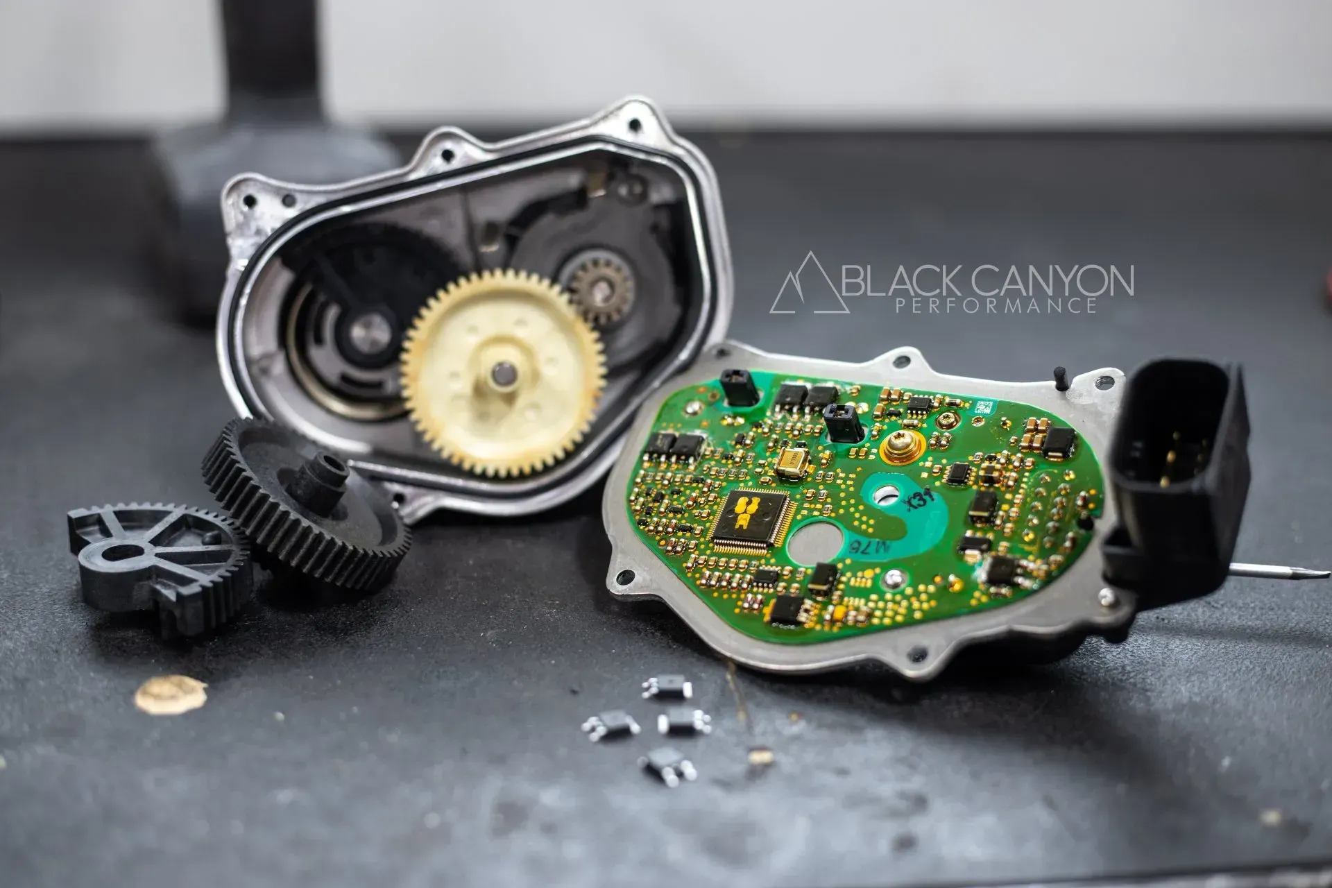 Disassembled mechanical device with exposed gears and green circuit board on a dark surface