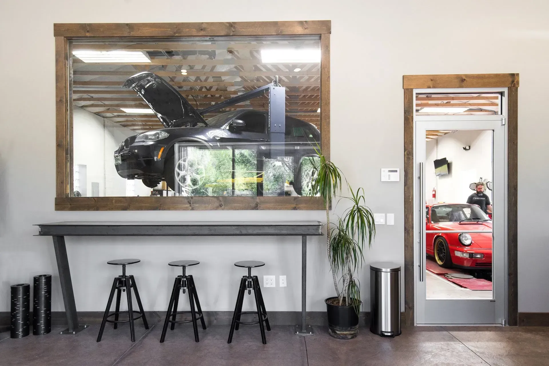 Modern lobby with large wall mirror, three stools, potted plant, and a doorway reflecting a red car outside
