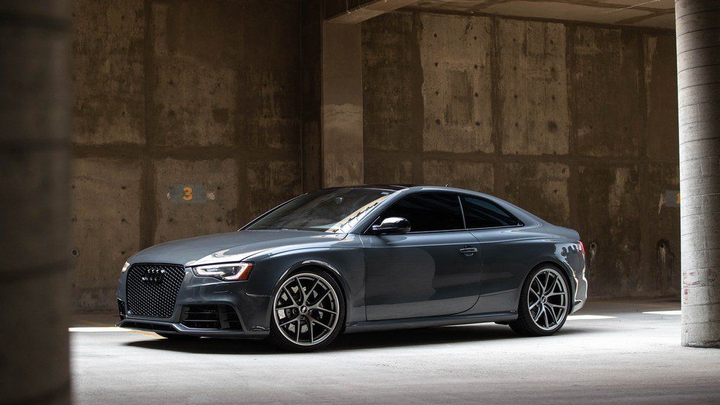 Dark gray sports coupe parked in an industrial concrete garage.